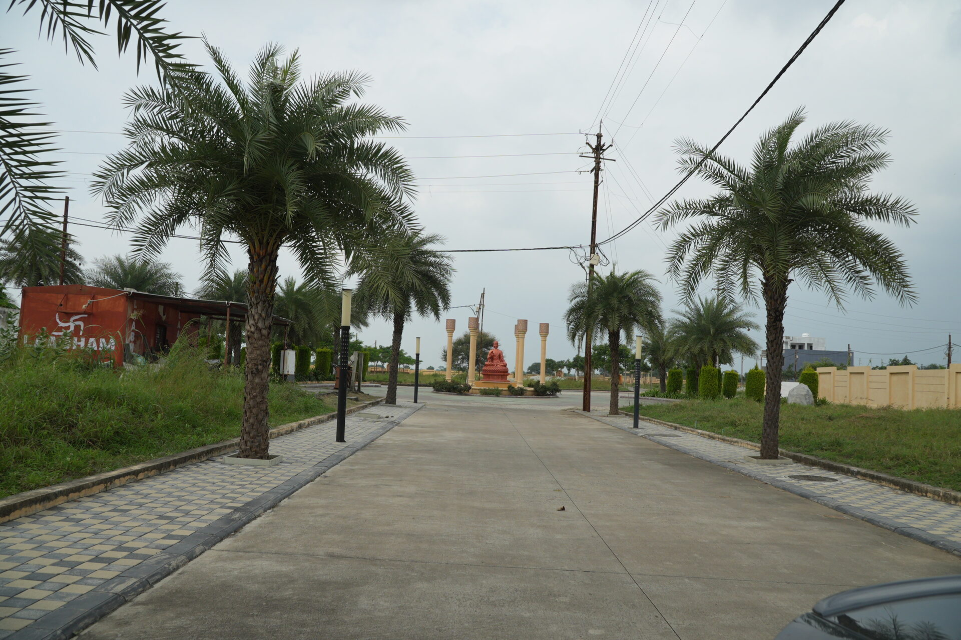 A paved internal road at Labham City on Super Corridor, lined with date palms and street lamps, running towards the entrance.
