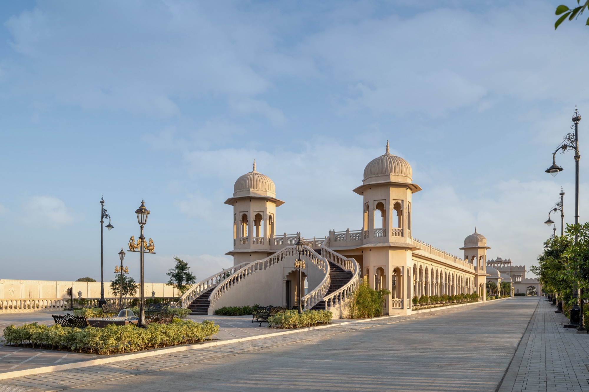A long colonnaded pavilion with domed chhatris and a twin staircase, ornamental street lamps and planted beds beside a paved internal road at Oscar Palace.