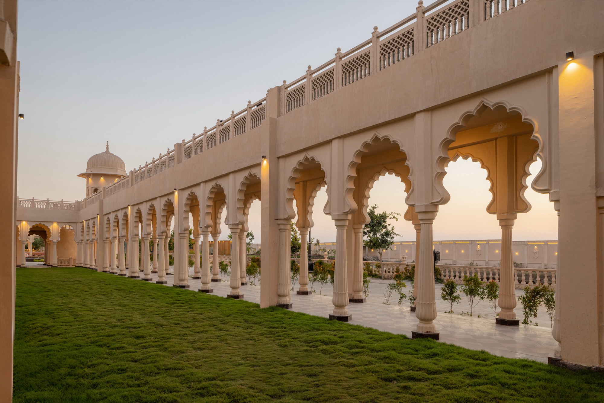 The arcaded walkway at Oscar Palace at dusk: scalloped stone arches on slim columns running beside a lawn, with a domed pavilion at the far end.